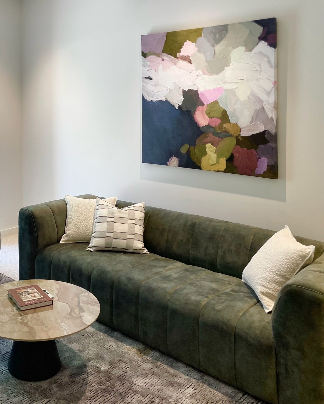 Olive-green velvet sofa beneath a layered abstract canvas in the lounge