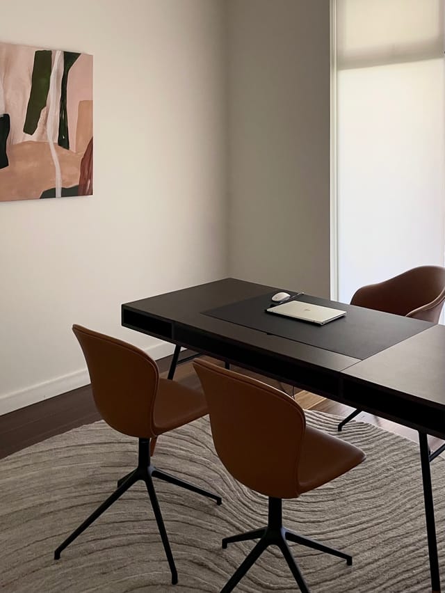 Study with tan leather chairs, dark timber desk, and pink abstract canvas